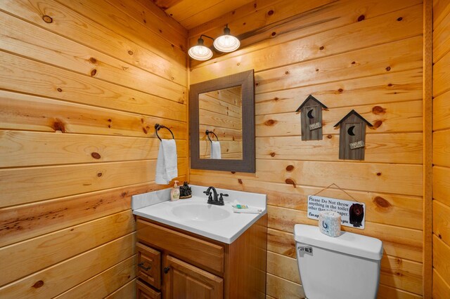 bathroom featuring toilet, wood walls, and vanity