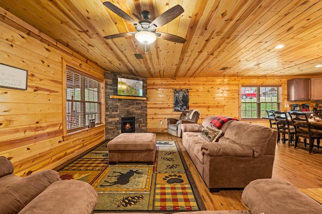 living area featuring light wood finished floors, ceiling fan, a stone fireplace, wood ceiling, and wood walls