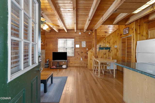 living area with beam ceiling, a ceiling fan, wood walls, wooden ceiling, and hardwood / wood-style floors