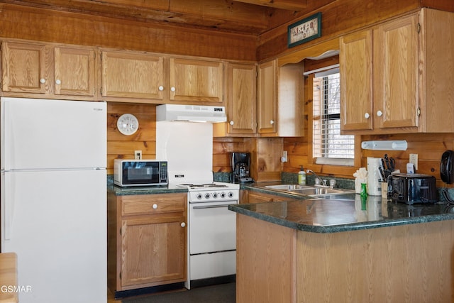 kitchen featuring under cabinet range hood, a peninsula, white appliances, wood walls, and a sink