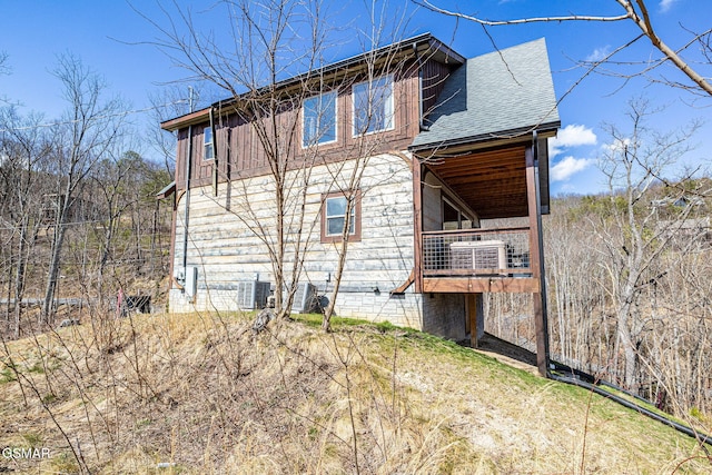 rear view of house with cooling unit, a shingled roof, and a balcony