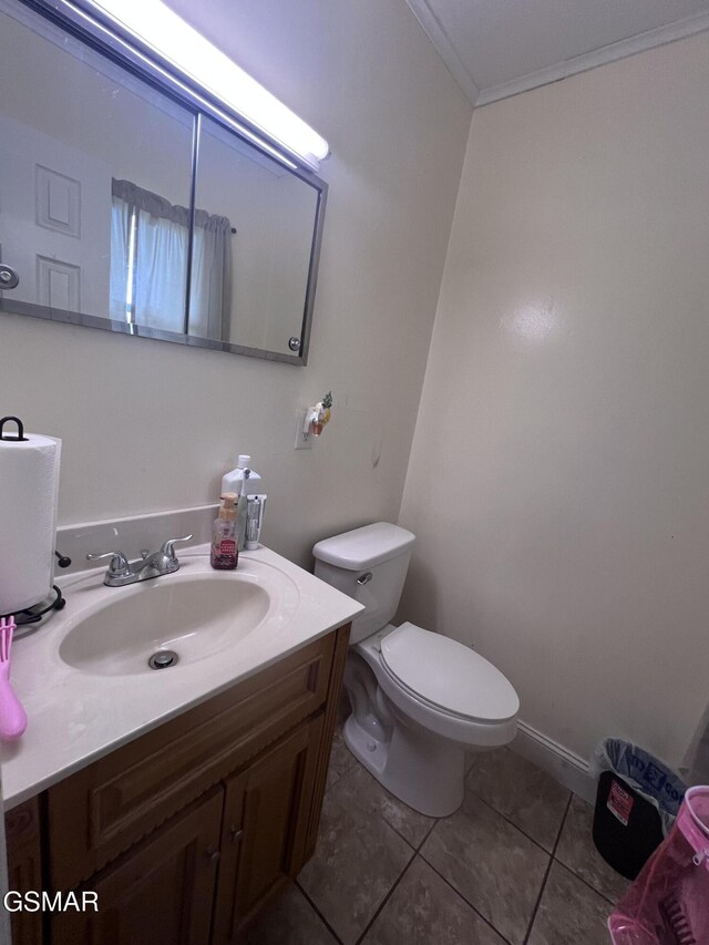 half bath with toilet, vanity, ornamental molding, and tile patterned flooring