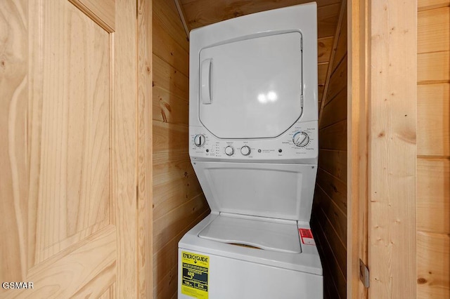 clothes washing area featuring stacked washer / drying machine and wood walls