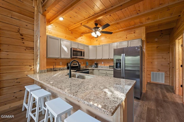 kitchen featuring beam ceiling, light stone countertops, kitchen peninsula, a breakfast bar area, and appliances with stainless steel finishes