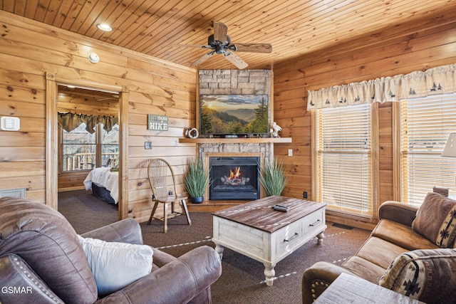 living room with ceiling fan, dark colored carpet, wood ceiling, and a fireplace