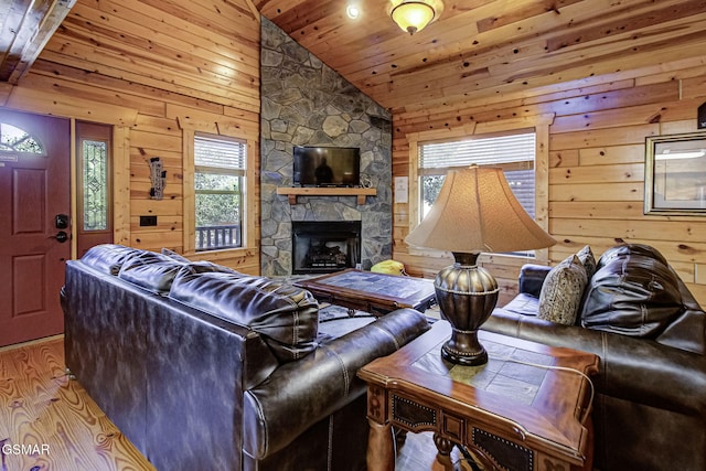 living room featuring a stone fireplace, high vaulted ceiling, wood walls, wooden ceiling, and light wood-type flooring