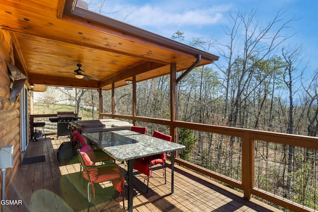 wooden deck featuring outdoor dining space, ceiling fan, grilling area, and a wooded view