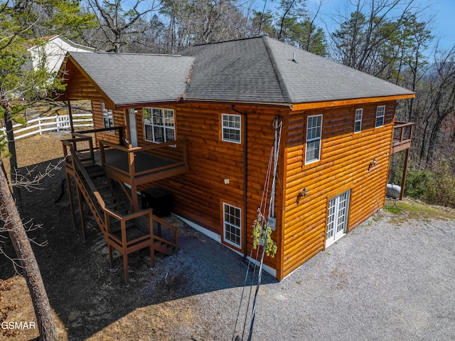 back of house with gravel driveway, a shingled roof, faux log siding, and stairs