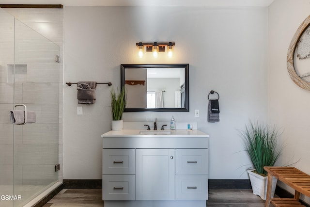 full bath with wood finished floors, a shower stall, vanity, and baseboards