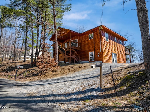 view of property exterior featuring a deck, log veneer siding, driveway, and stairway