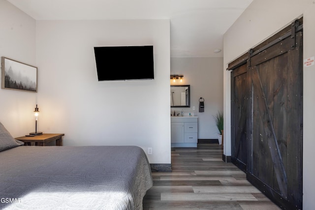 bedroom featuring ensuite bathroom, a barn door, a sink, wood finished floors, and indoor wet bar