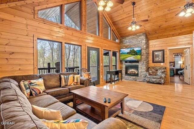 living room with ceiling fan, wooden walls, hardwood / wood-style flooring, high vaulted ceiling, and a fireplace