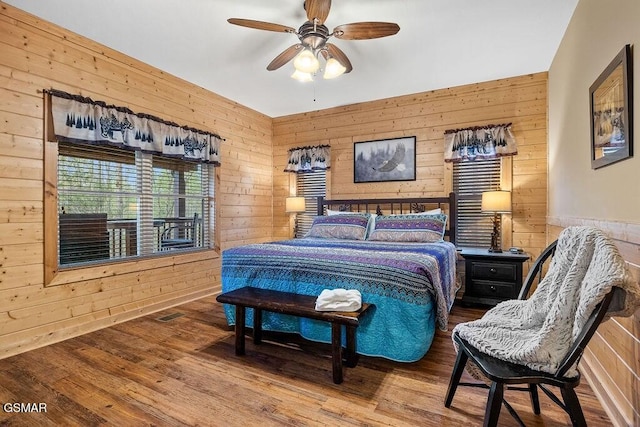 bedroom with hardwood / wood-style flooring, ceiling fan, and wooden walls