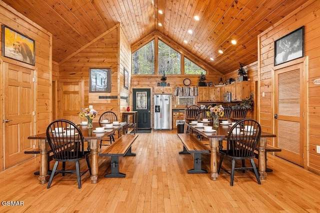 dining area with light hardwood / wood-style floors, high vaulted ceiling, wood walls, and wood ceiling