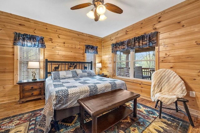 bedroom with ceiling fan, wood-type flooring, wooden walls, and multiple windows