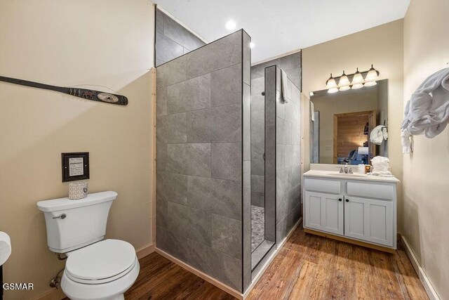 bathroom with tiled shower, vanity, hardwood / wood-style flooring, and toilet