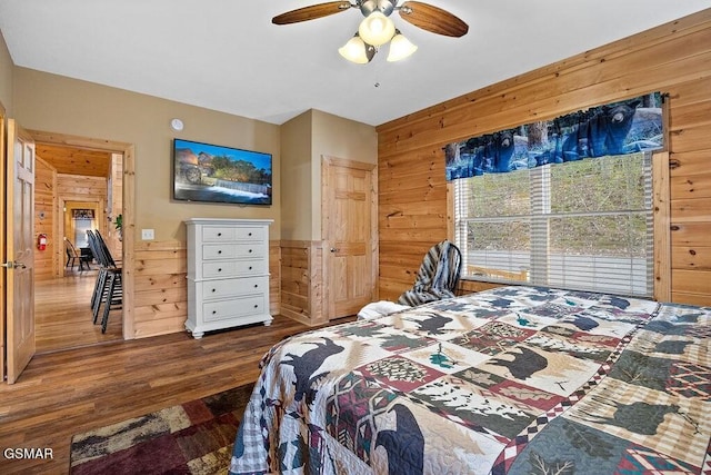 bedroom with ceiling fan, dark wood-type flooring, and wood walls