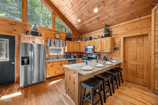 kitchen featuring sink, wooden walls, light hardwood / wood-style flooring, appliances with stainless steel finishes, and light stone counters