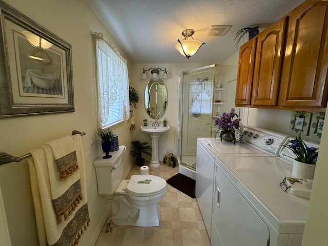 bathroom with washing machine and clothes dryer, a shower with shower door, a textured ceiling, and toilet