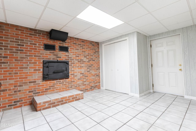 unfurnished living room featuring a drop ceiling, light tile patterned floors, and brick wall