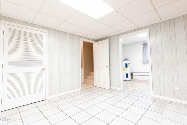 tiled spare room with a drop ceiling, wooden walls, and water heater