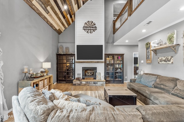 living area with a large fireplace, visible vents, high vaulted ceiling, and wood finished floors