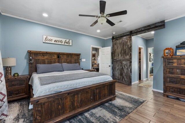 bedroom featuring crown molding, a spacious closet, visible vents, a barn door, and wood finished floors