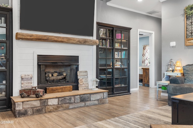 living area featuring visible vents, baseboards, ornamental molding, wood finished floors, and a large fireplace