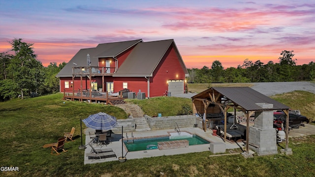 back of property at dusk featuring a balcony, an outdoor pool, a garage, a yard, and a deck