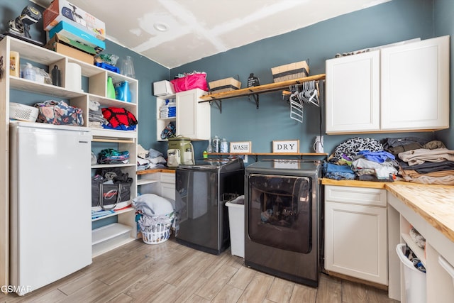 clothes washing area featuring cabinet space, light wood-style flooring, and washing machine and dryer