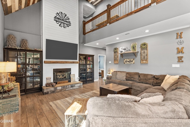 living room featuring a large fireplace, visible vents, recessed lighting, a high ceiling, and hardwood / wood-style flooring