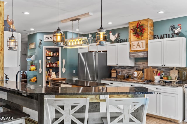 kitchen with white cabinets, freestanding refrigerator, a breakfast bar, crown molding, and backsplash