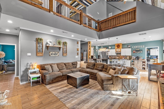 living area featuring recessed lighting, a towering ceiling, light wood-style flooring, and visible vents