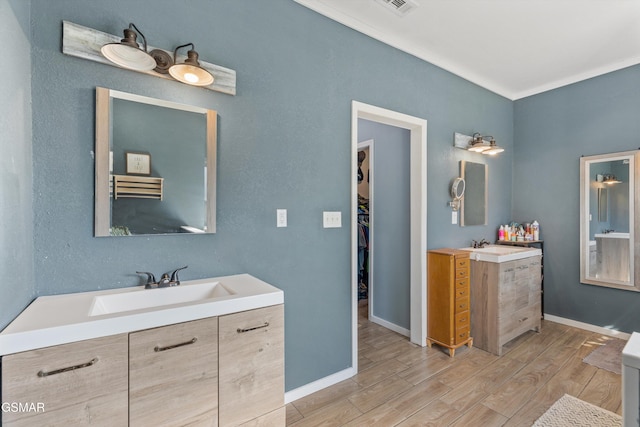 full bathroom featuring two vanities, wood finished floors, a sink, and baseboards
