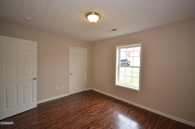 unfurnished bedroom featuring visible vents, baseboards, a textured ceiling, and dark wood-style flooring