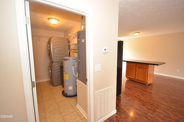 utilities featuring visible vents, electric water heater, and stacked washing maching and dryer