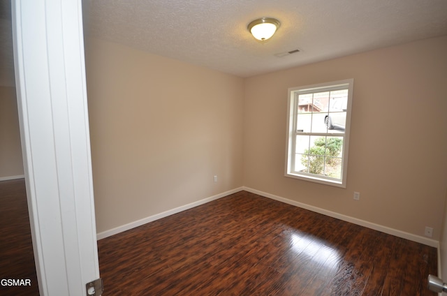 spare room with dark wood finished floors, visible vents, a textured ceiling, and baseboards