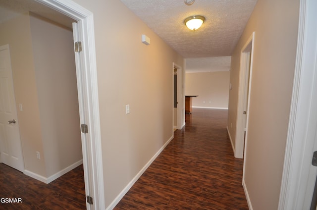 hall with dark wood finished floors, baseboards, and a textured ceiling