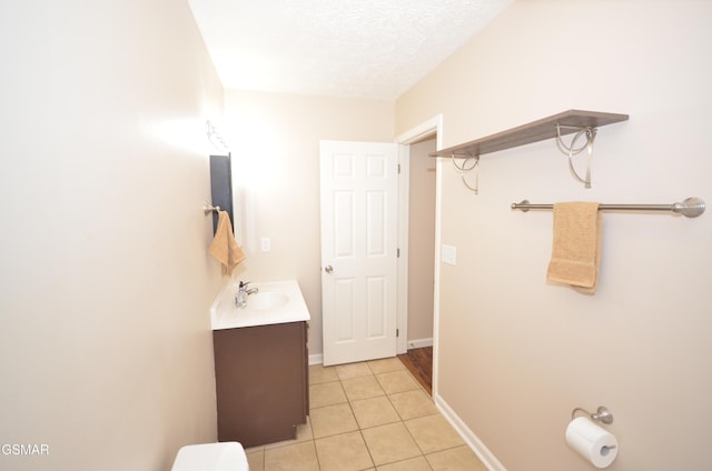 bathroom featuring tile patterned flooring, baseboards, toilet, vanity, and a textured ceiling