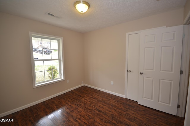 unfurnished room with visible vents, baseboards, dark wood-type flooring, and a textured ceiling