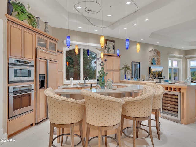 kitchen with paneled built in fridge, a raised ceiling, double oven, a kitchen island with sink, and beverage cooler