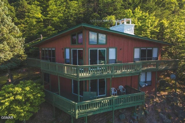 rear view of house with a forest view, a chimney, and a wooden deck