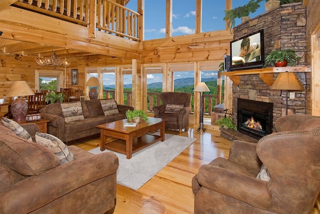 living room with a chandelier, a stone fireplace, a towering ceiling, and light hardwood / wood-style flooring