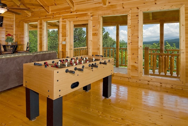 recreation room featuring beam ceiling, light hardwood / wood-style flooring, ceiling fan, and wood walls