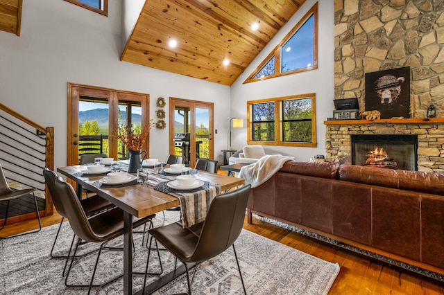 dining space with french doors, high vaulted ceiling, wooden ceiling, hardwood / wood-style floors, and a stone fireplace