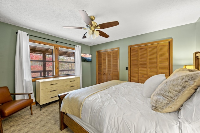 carpeted bedroom featuring a textured ceiling, two closets, and ceiling fan