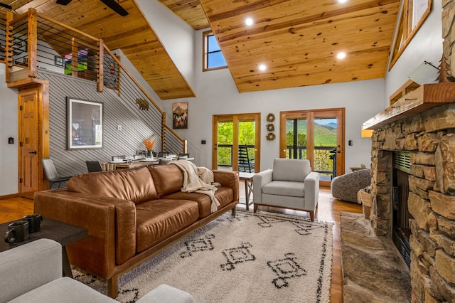 living room featuring a stone fireplace, ceiling fan, a towering ceiling, and light wood-type flooring