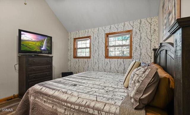 bedroom featuring lofted ceiling, baseboards, wood finished floors, and wallpapered walls