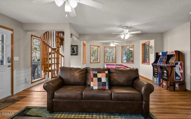 living area with stairs, a textured ceiling, wood finished floors, and a ceiling fan