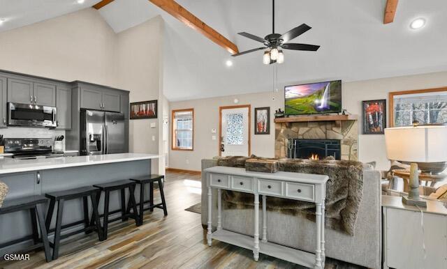 kitchen with gray cabinetry, a breakfast bar, light countertops, appliances with stainless steel finishes, and dark wood-style floors